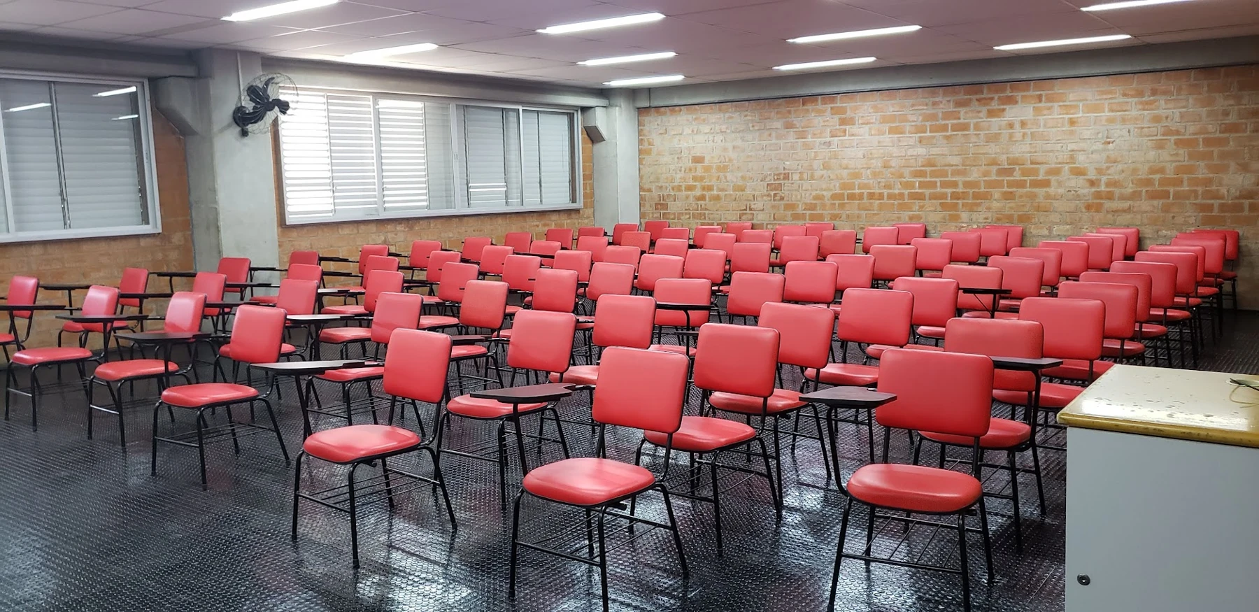 Auditório com fileiras de cadeiras reformadas em vermelho